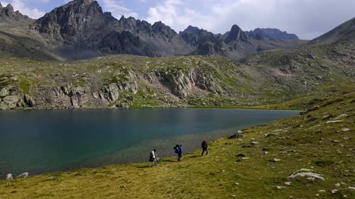 Hikers Traverse by an Alpine Lake in Mountains