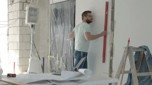 Architekt inspiziert Wohnungswand mit Ebene und Bauplänen im Innenbereich