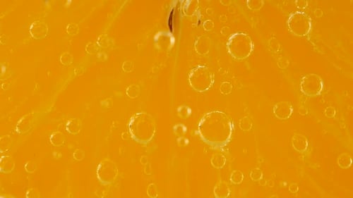 Eine Scheibe reifer Orange im Wasser sprudelt auf einem orangefarbenen Hintergrund.