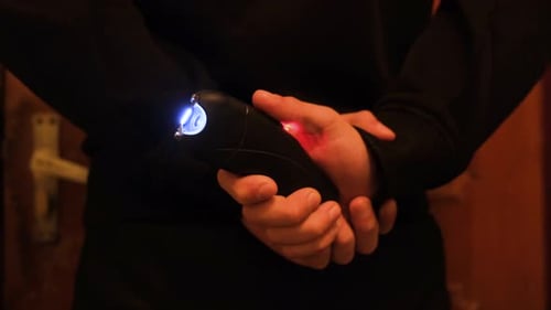 A Man Holds a Stun Gun Behind His Back Pressing the Button and Triggering an Electric Discharge A