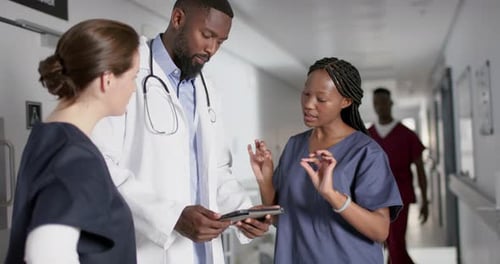 Diverse male and female doctors discussing work, using tablet in corridor at hospital, slow motion