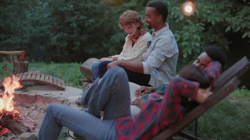 Friends Relaxing by a Campfire at Night in a Forest Setting