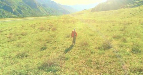 Flight Over Backpack Hiking Tourist Walking Across Green Mountain Field Huge Rural Valley at Summer
