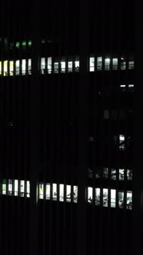 Vertical drone shot around office windows on a corporate building, night darkness