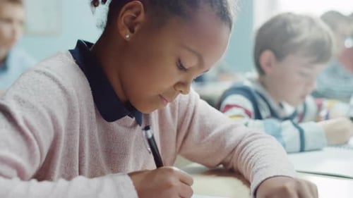 In Elementary School Classroom Girl Writes in Exercise Notebook, Taking Test. Junior Classroom with