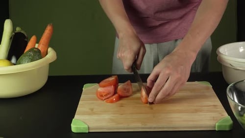 Hands of middle man european slices a tomato with kitchen knife on cutting board, front side view