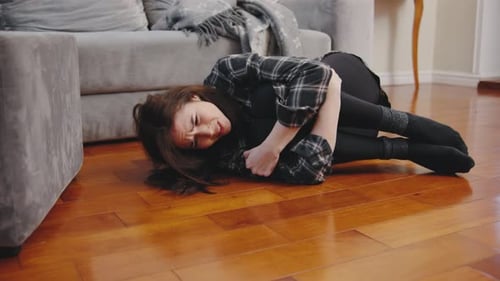 Une jeune femme en détresse est allongée sur le sol dans un appartement confortable, recroquevillée en position foetale et