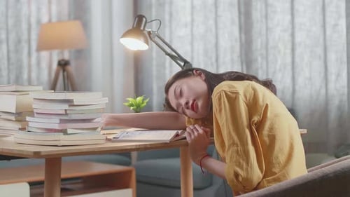 Side View Of Young Asian Female Studying At Home Sleeping While Reading Books On The Table