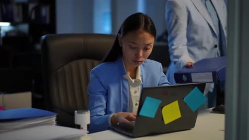 Asian Woman Working in Office As Caucasian Colleague Passing Bringing Paperwork
