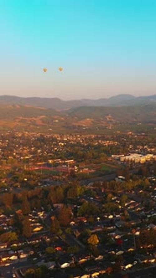 Hot air balloons flying over the beautiful city. Sunlit scenery of Napa, California, USA
