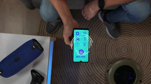 Top View Close Up Shot of Man on the Sofa Holding Smartphone Using App to Switch on Music Speaker