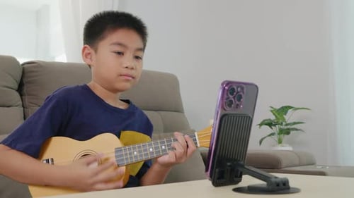 Boy Plays Ukulele While Watching Mobile Phone