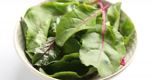 Spraying fresh beetroot leaves with water at white table, closeup