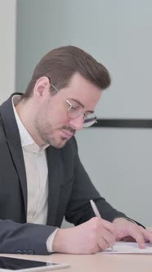 Man in Suit Signing Document at Desk Indoors