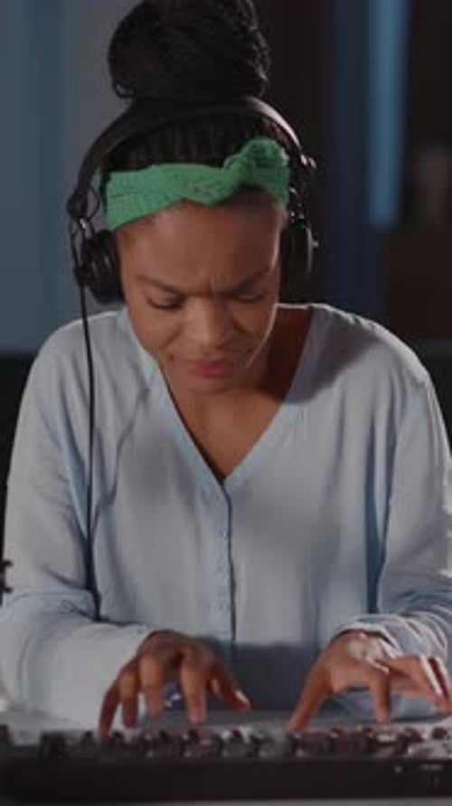 A Woman in Headphones and a Green Headband Joyfully Plays a Keyboard