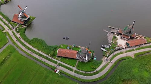 A stunning aerial view of traditional Dutch windmills beside a winding canal, with red-roofed houses