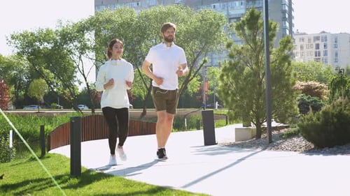 Happy Caucasian Young Male and Female Joggers Jogging Together on Sunny Summer Day in Sportswear