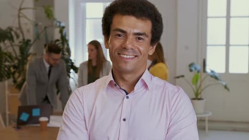 Portrait of smiling businessman in office with his colleagues in background.