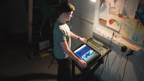 Young Adult Manipulates Technical Console in Dark Workspace