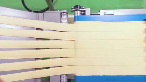 Actual shot of mechanized assembly line rolling out strips of dough leftovers transported by conveyo