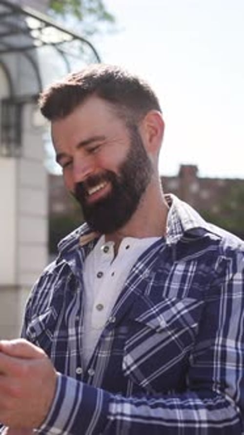 Bearded Man Smiling At Phone In Urban Setting
