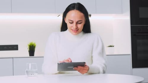 Une jeune femme joyeuse parcourt des pages Web sur une tablette en souriant
