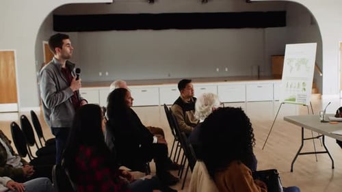Man In Audience Asking Question Of Community Leaders In Town Hall