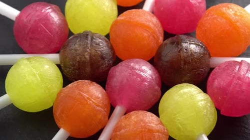 Colorful lollipops or candy bonbons on a stick rotating on black plate close up top view. Holiday