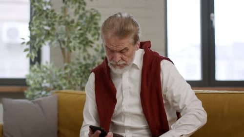 Serious Senior Man Sitting at Phone and Answering Phone Call Enjoying Pleasure Talk with Old Friend