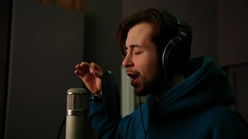 Rap singer with headphones and microphone emotionally recording new song in professional studio
