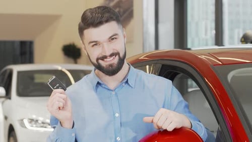 Joyful Man Proudly Displaying Car Keys at a Sleek Dealership Showroom