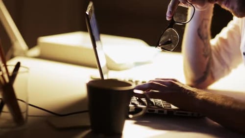 Man Types on Laptop at Desk at Night