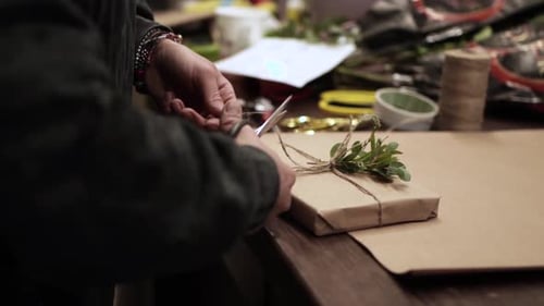Craftsperson Decorates Wrapped Gift with Twine and Greenery