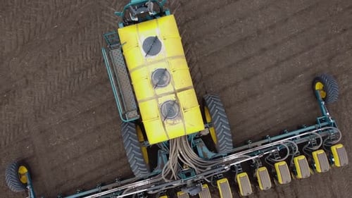 Blue tractor with yellow seeder working on the field in Ukraine OA