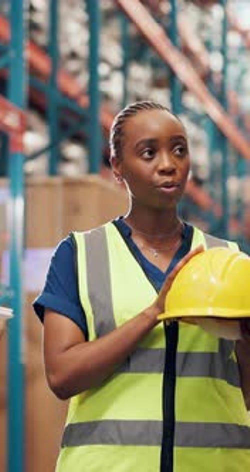 Woman, team and talk at warehouse for helmet for safety training, info and explain with vest