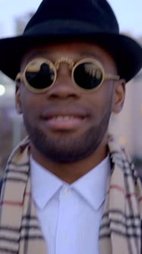 A Stylish Urban Man is Wearing Trendy Sunglasses and a Fashionable Hat While in the City