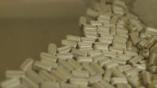 lot of rectangular beige lollipops slide down a metal plate in a candy factory