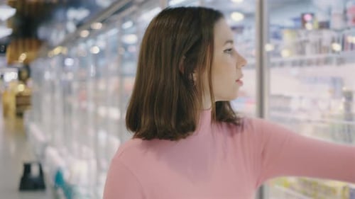 A Customer in a Pink Sweater is Shopping in the Dairy Section of a Grocery Store Browsing and