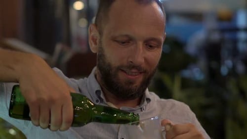 Happy young man enjoys refreshing beer and relaxation in a city cafe at night