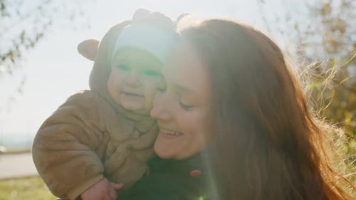 Smiling Woman Holds Infant in Bear Suit Outdoors
