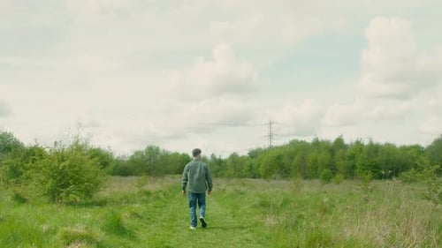 Man Walks Alone Through Tall Grass Under Cloudy Sky