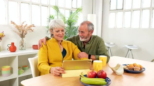 Senior Couple Smiling at Tablet Device at Home