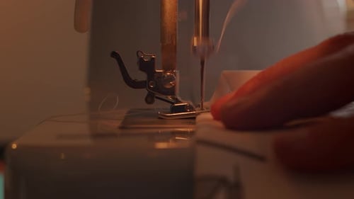 Side close view of slow motion needle of sewing and hands moving fabric as it is sewed.