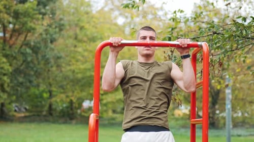 Sporty young man doing pull-ups on piece of sports equipment in public park, tracking shot