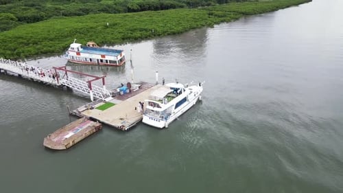 Flying new small river cruise ship docked on jetty in river with buildings and red bridge in backgro