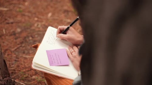 From above footage of woman writing in her personal diary while seated in forest at Canada, with gro