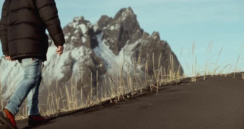Man Traversing Black Sand With Snowy Mountains In View