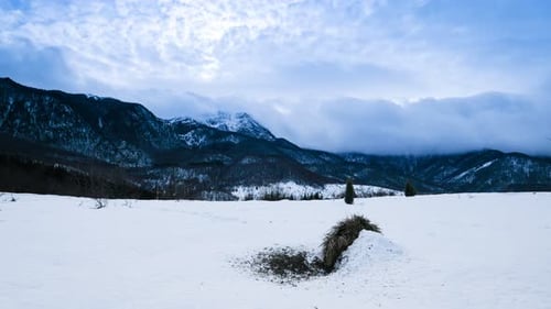 Time lapse of snowy landscape with mountains shrouded in clouds showcasing a tranquil winter scene
