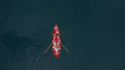Top down aerial view of a people paddling in a red paddling boat on the deep turquoise alpine lake T