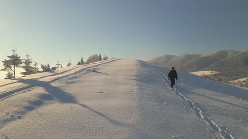 Aerial View of Backpacker Hiking Snowy Mountain Hillside on Cold Winter Morning